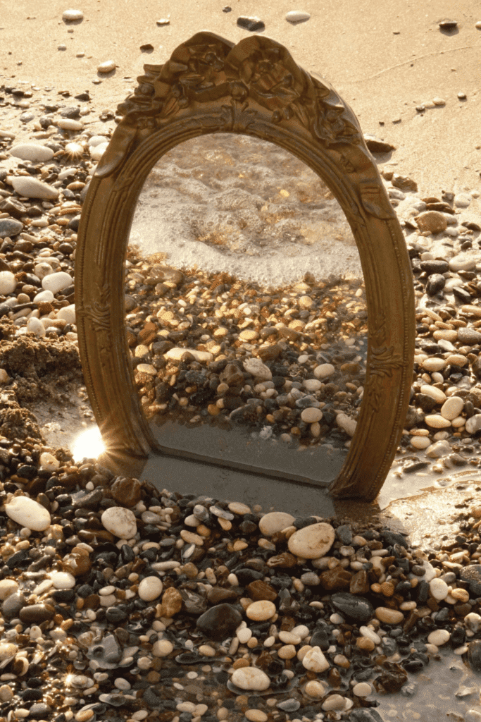 A mirror placed on a beach surrounded by many seashells.