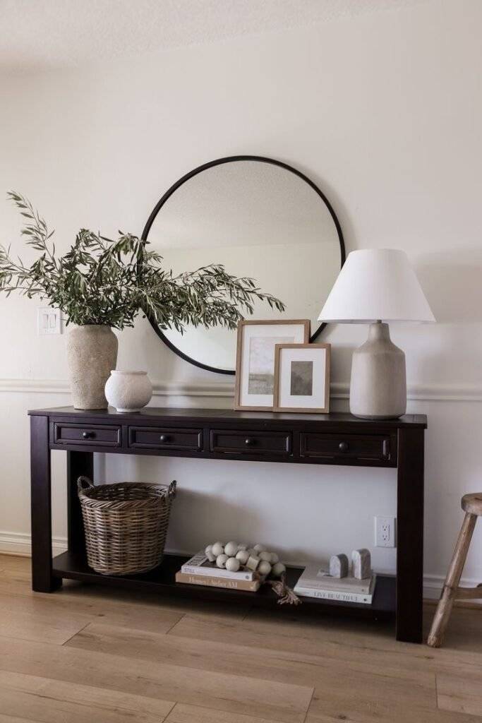 Black wooden console table with vases and a round mirror.