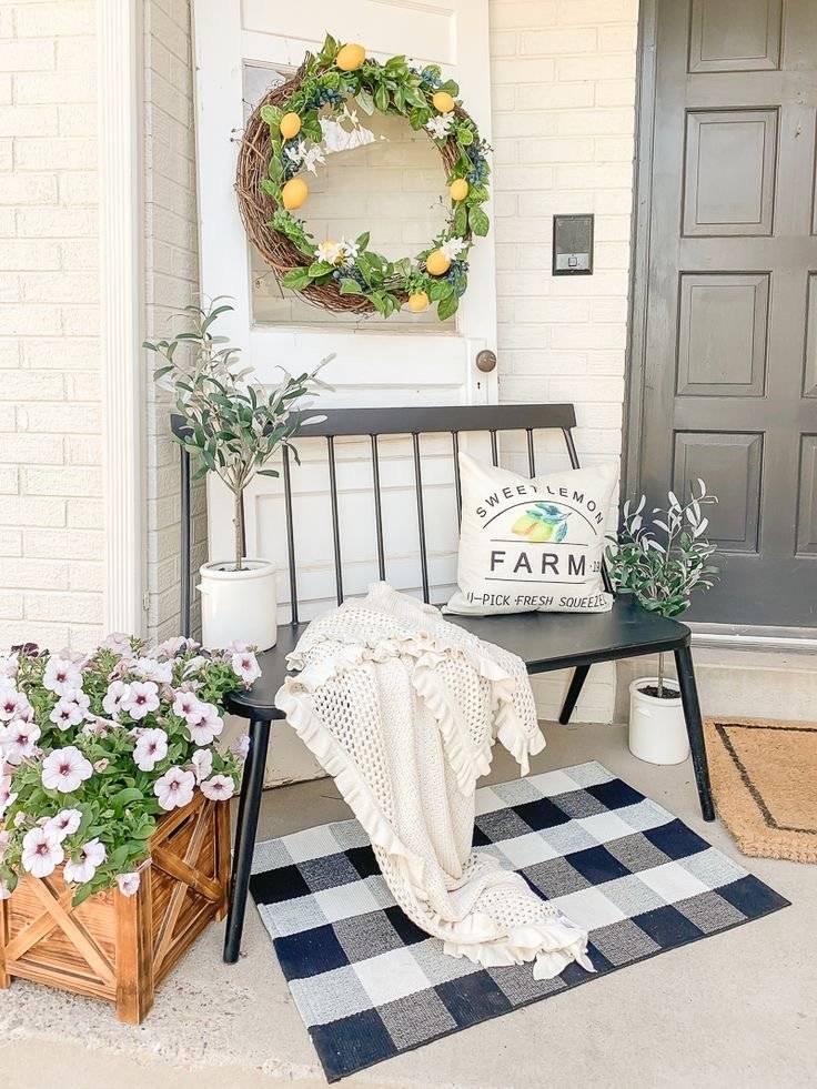 A white decorative wooden door with lemon and flower wreath behind black metal bench.