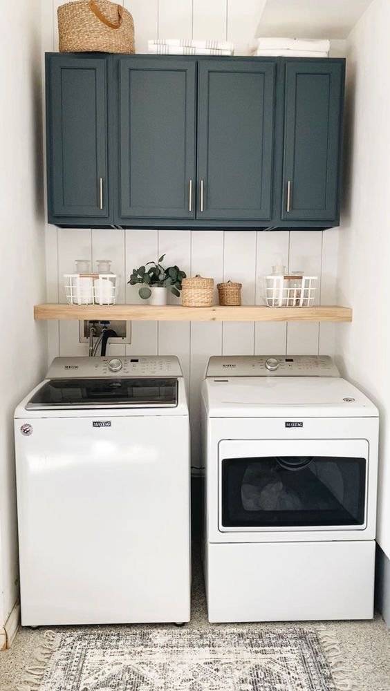 A blue laundry cabinet with a wooden floating shelf.