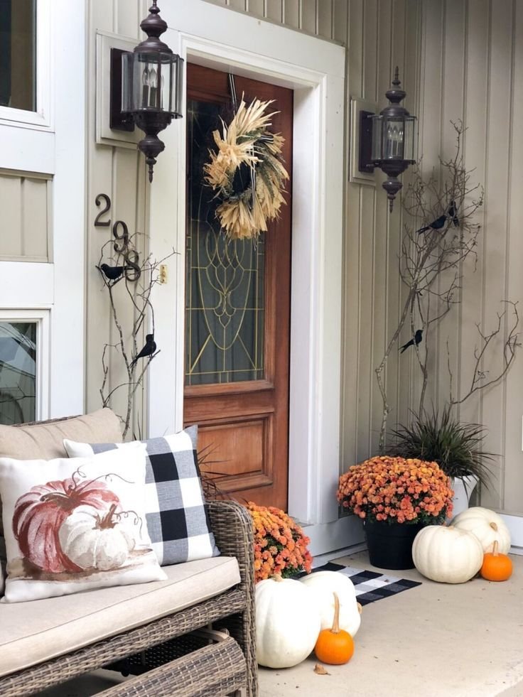 A wooden door with a fall wreath. This front porch decor has branches with fake crows, chrysanthemums and pumpkins.