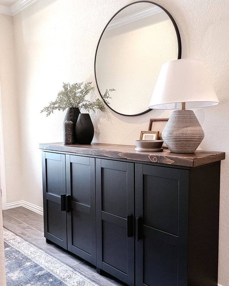 A black entryway cabinet with a round mirror.