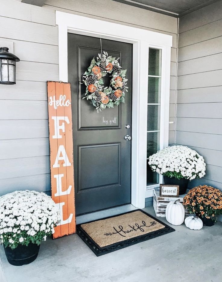 A black door with a fall wreath, a fall wooden sign and chrysanthemums.