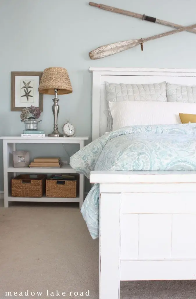 A beach house bedroom with wooden furniture, a blue and white color palette and coastal items.