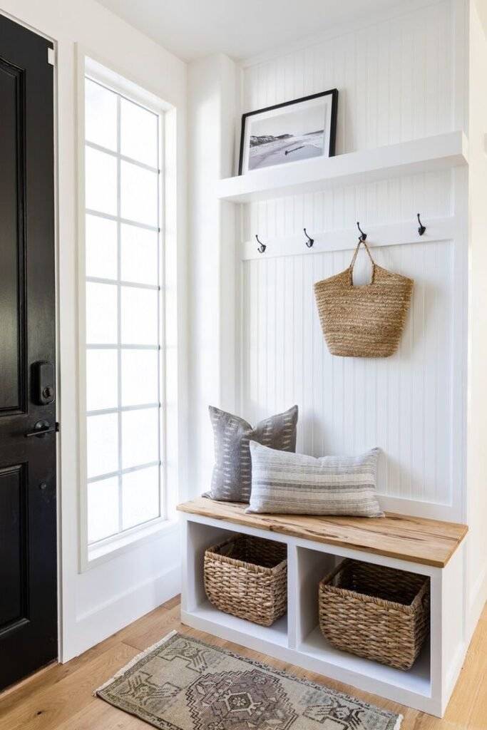 White wall with black metal hooks and wooden bench with woven baskets.