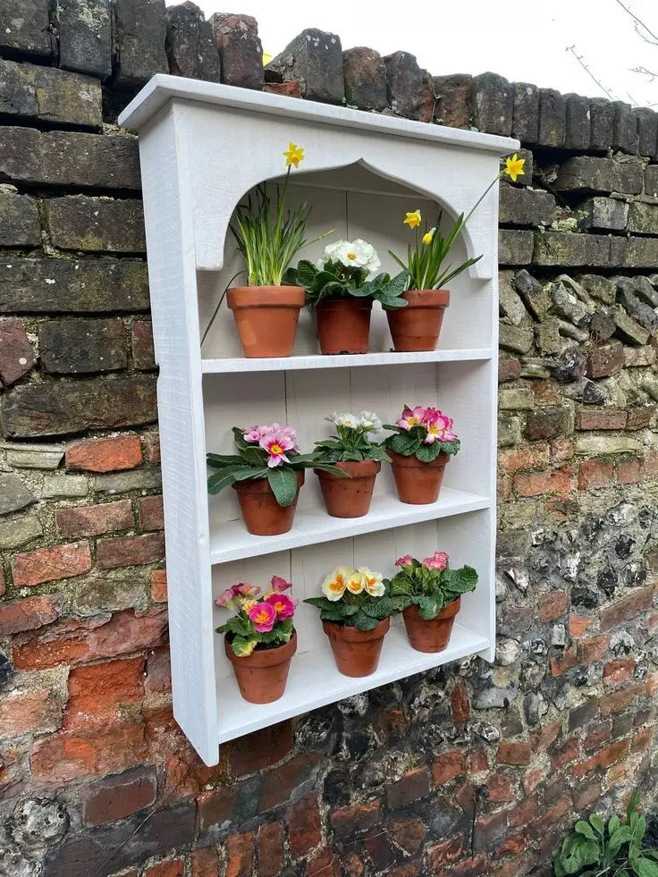 A shelf placed on a garden fence filled with flowers.