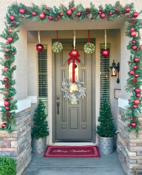 A gray door with a Christmas wreath, a winter garland and ornaments hanging from the wall.