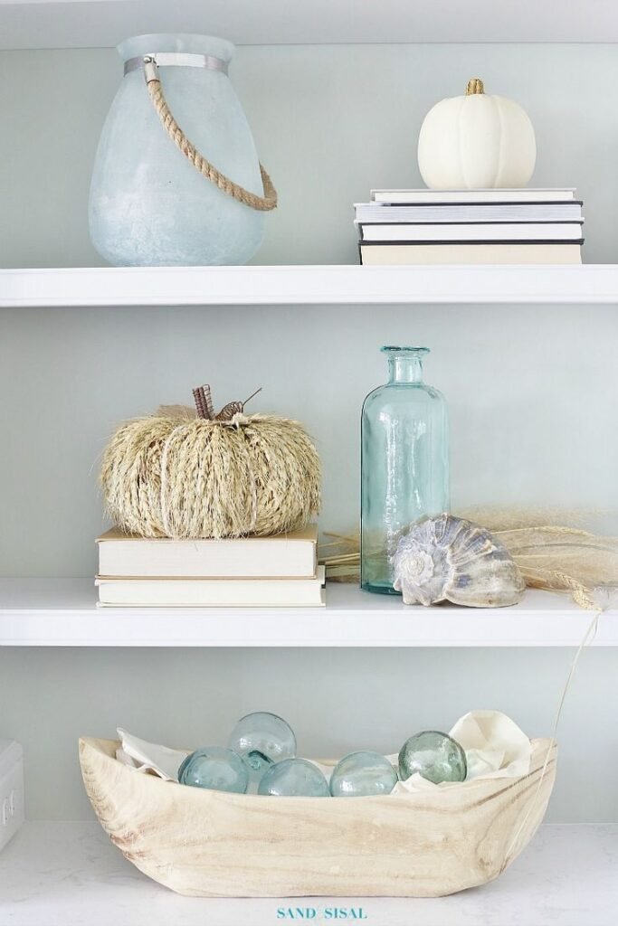 An open shelf filled with coastal items and pumpkins.