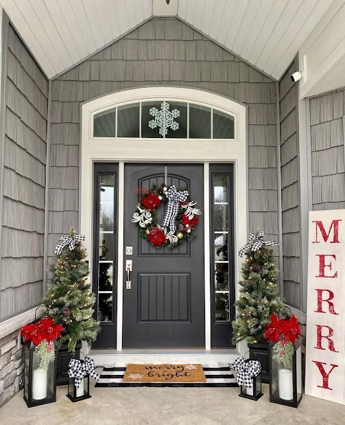 A gray door with a Christmas wreath, a merry wooden sign, Christmas trees and lamps.