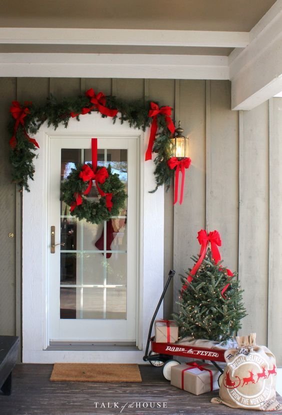 A white door with a Christmas garland and wreath with red bows.