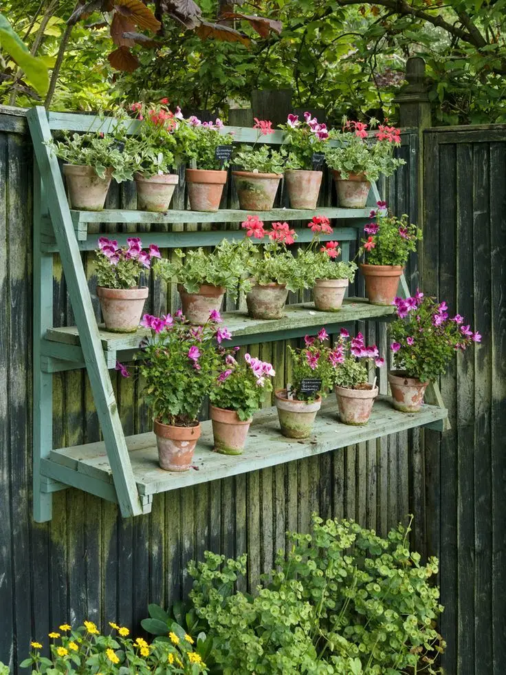 A hanging herb garden placed on a fence with many plant pots filled with flowers.