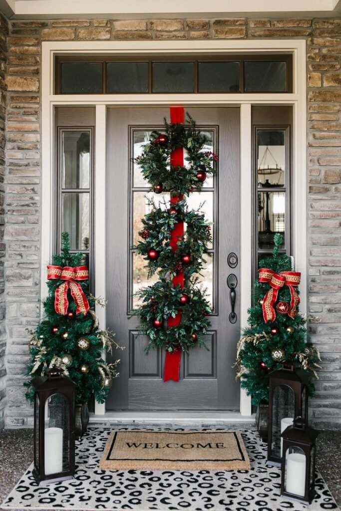 A gray door with three Christmas wreaths. This front porch decor has two Christmas trees with red bows, lamps and a welcome mat.