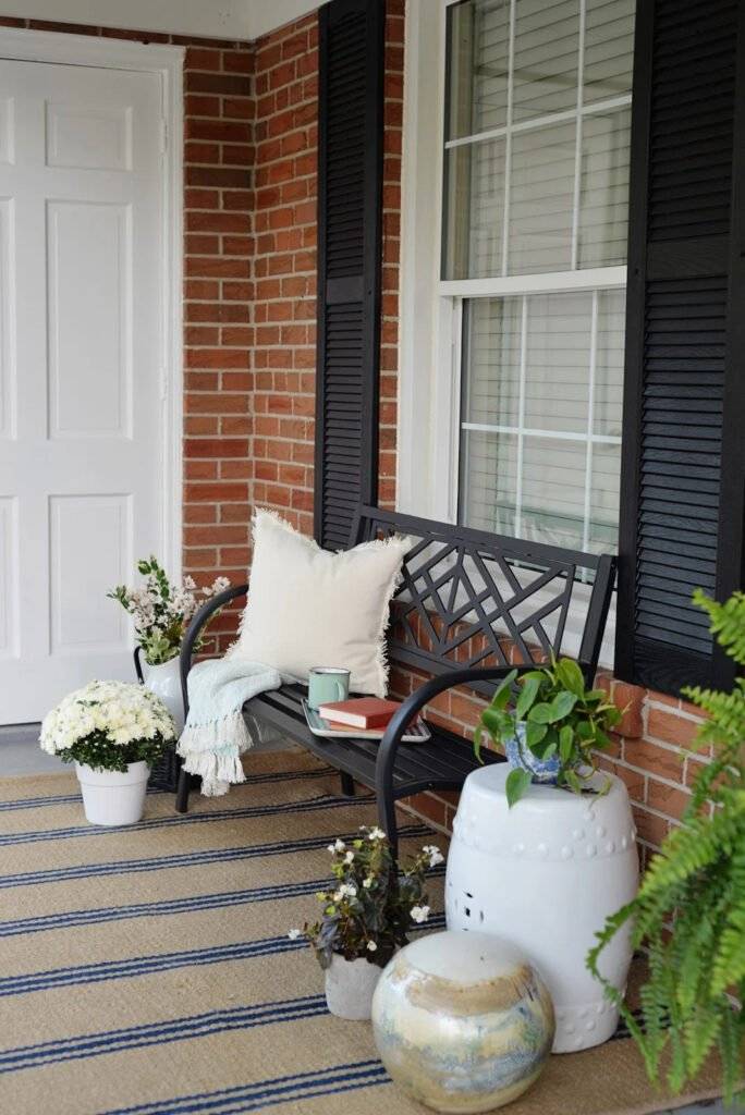 A porch decor with a black metal bench and plants.