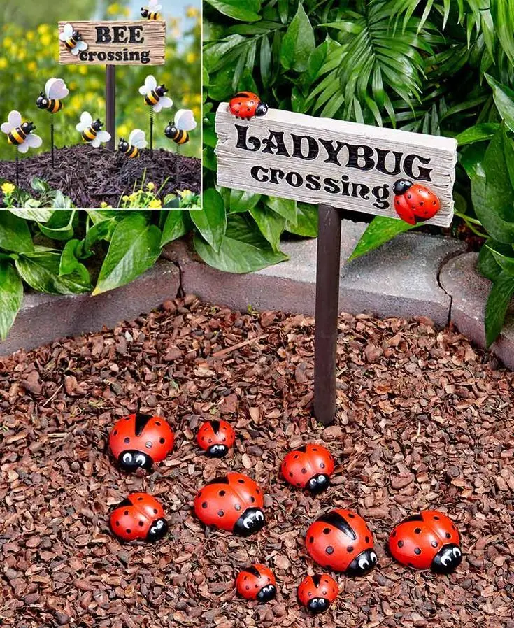 Rocks painted in lady bugs. The lady bugs are on the soil with a wooden sign saying "ladybug crossing".