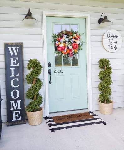 A blue front door with a spring wreath made of multicolor flowers. A welcome wooden sign is placed next to it as well as plants.