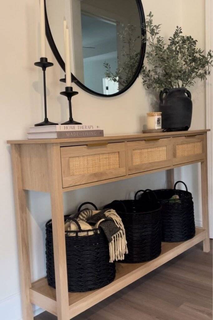 Black woven storage baskets with wooden console table and round black mirror.