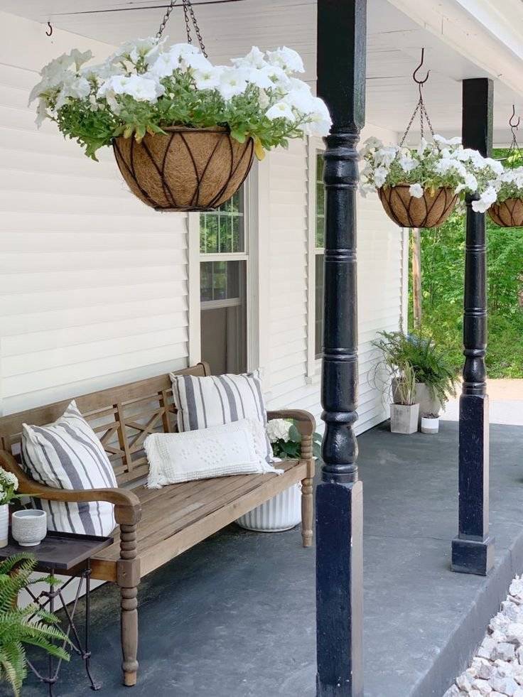 A porch decor with hanging baskets with white flowers and a wooden bench.