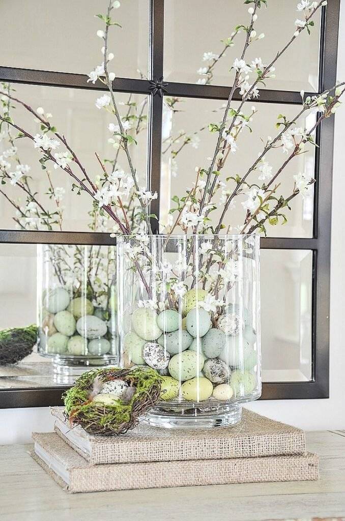 A glass container filled with Easter eggs and spring flower branches.