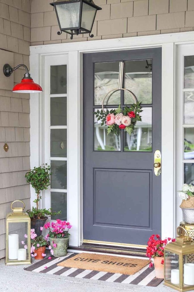 A gray front door with a spring wreath. This front porch decor is made of golden lamps and flowers.