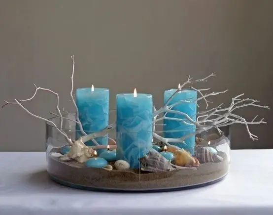 A coastal tray made of blue candles, sand and seashells.