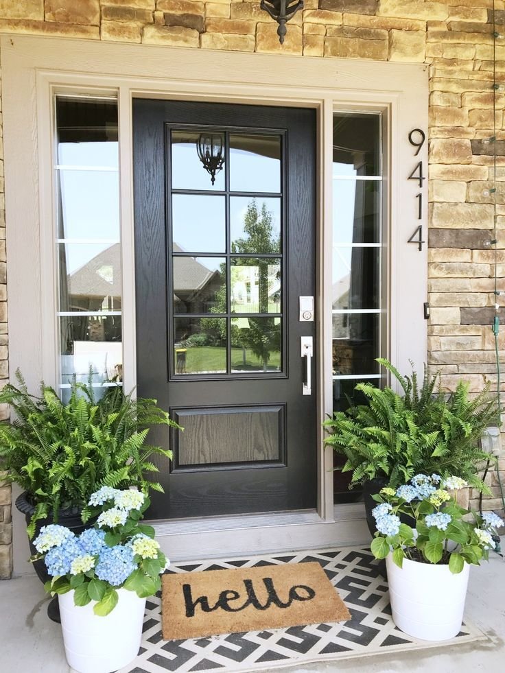 A black door with hydrangeas and a welcome mat.