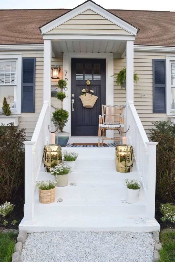 A black door with an hanging woven basket filled with flowers. It is a modern decor with neutral flower pots and golden stools.