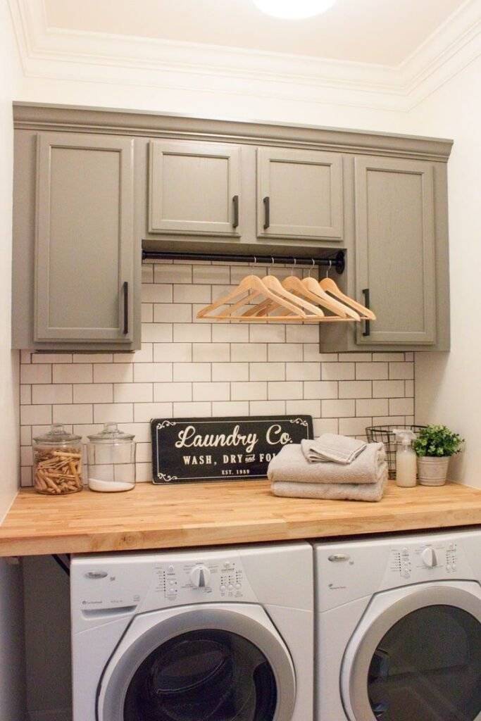 Sage green laundry cabinet, a hanging rod and a wooden countertop for a farmhouse look.