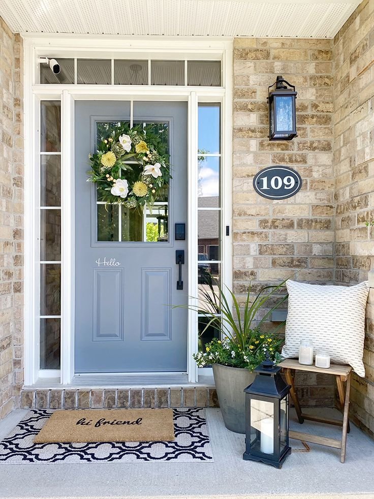 A gray door with a summer wreath, a welcome mat and a wooden stool.
