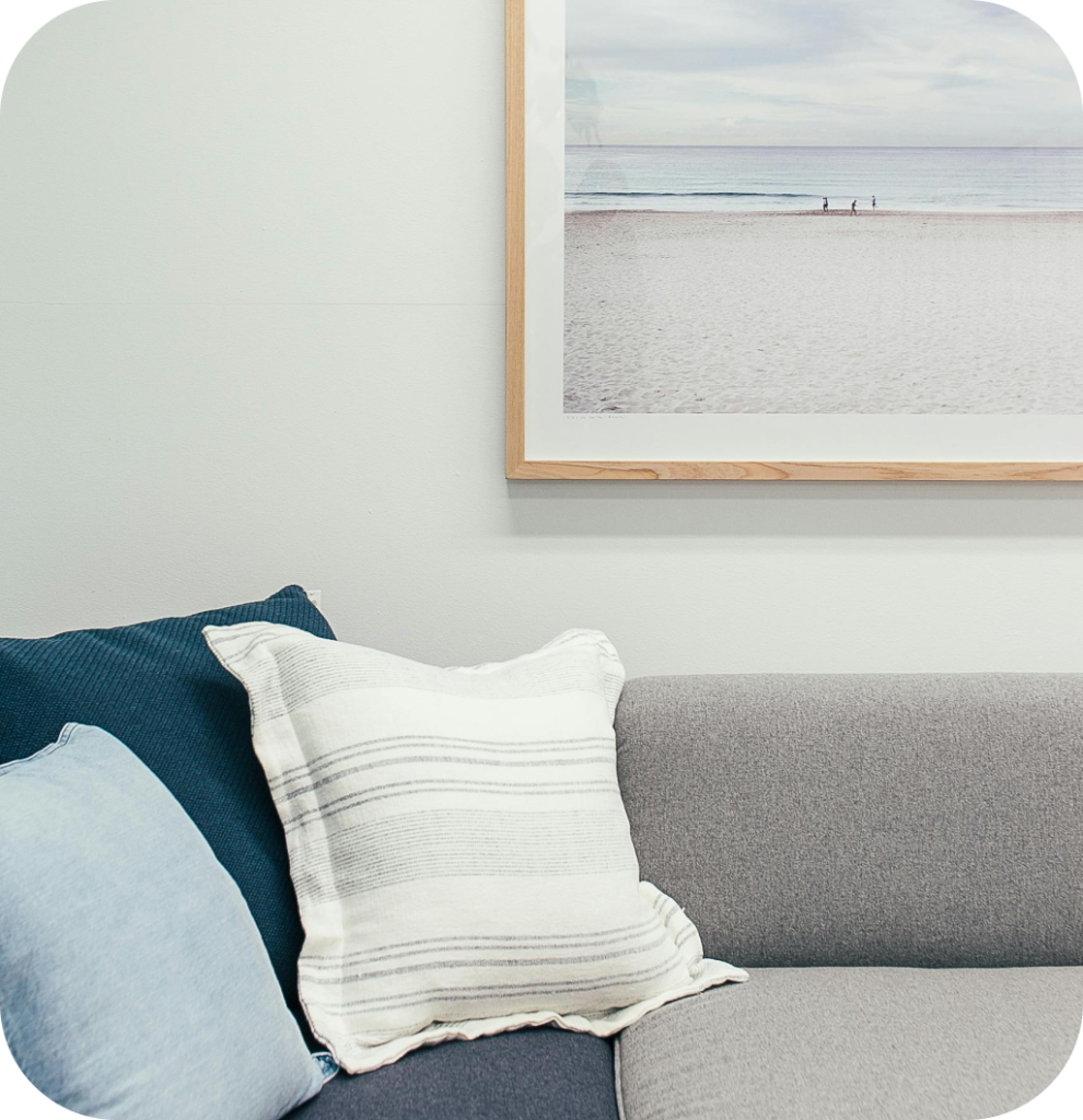 A coastal decor with blue pillows on a grey sofa with a beach frame.