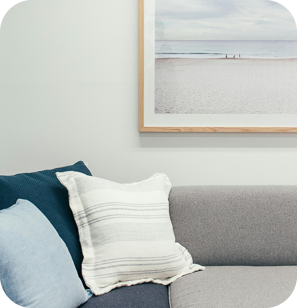 A coastal decor with blue pillows on a grey sofa with a beach frame.