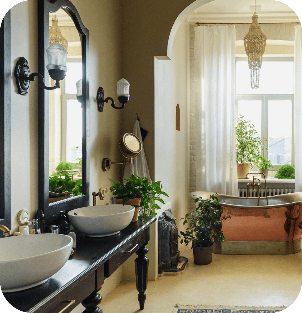 A farmhouse bathroom with a copper bath, a black mirror, two black lamps and a black bathroom cabinet with double sink.