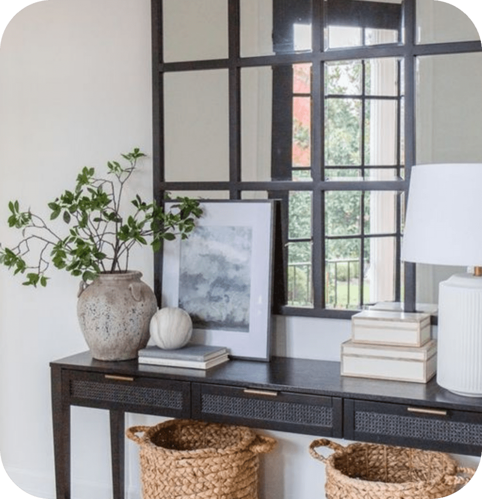 A black console table with woven baskets, a window pane mirror and vases.