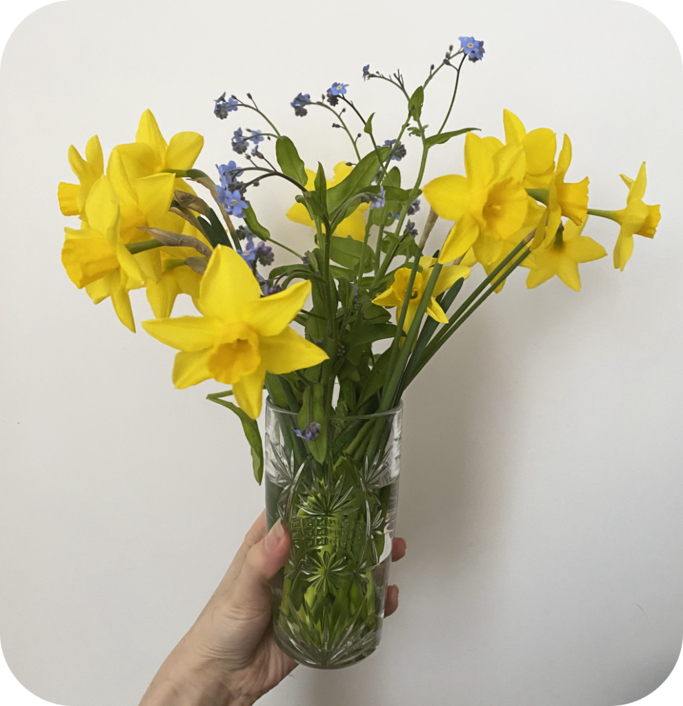 A glass vase filled with daffodils and purple flowers.