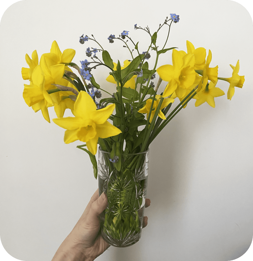A glass vase filled with daffodils and purple flowers.