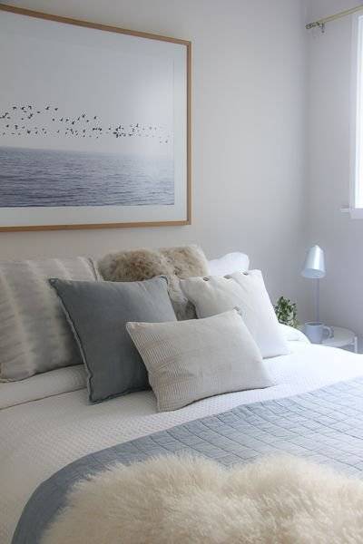 A framed picture of the sea above a white and grey blue bed.