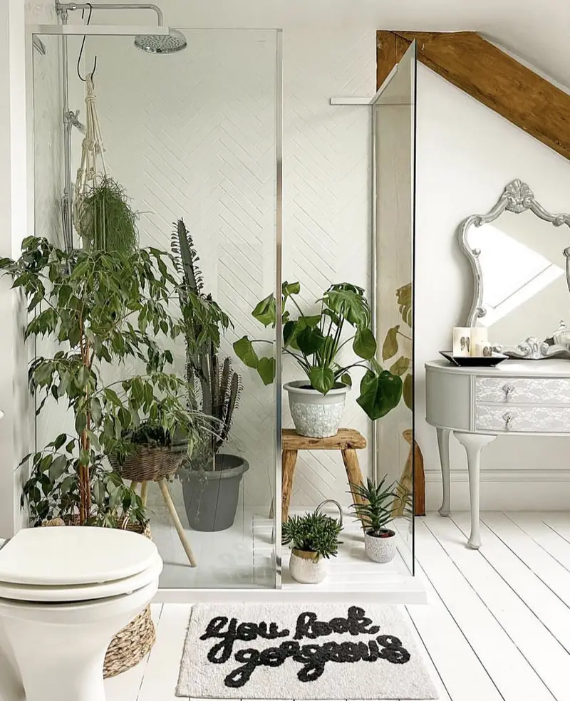 An antique gray mirror in a neutral bathroom with plants.