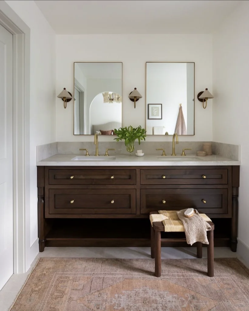 Two square mirrors with thin gold frames above a wooden bathroom cabinet with double sinks.