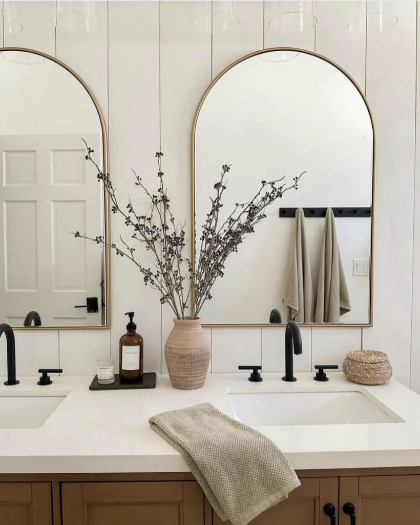 Two arched mirrors with thin gold frames above double sinks.