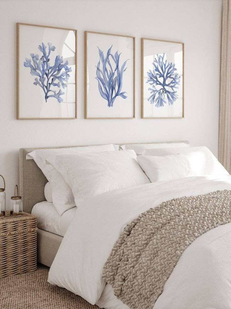 A white and beige bed with 3 blue coral watercolor illustrations framed above it.