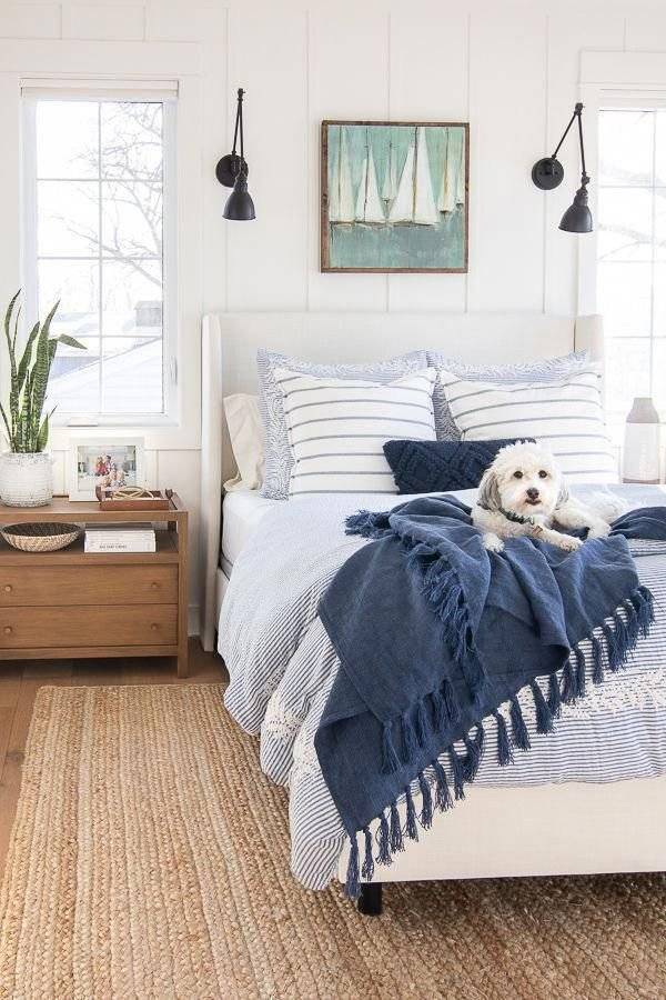 A white and blue bed with a boat canva and two black wall lamps.