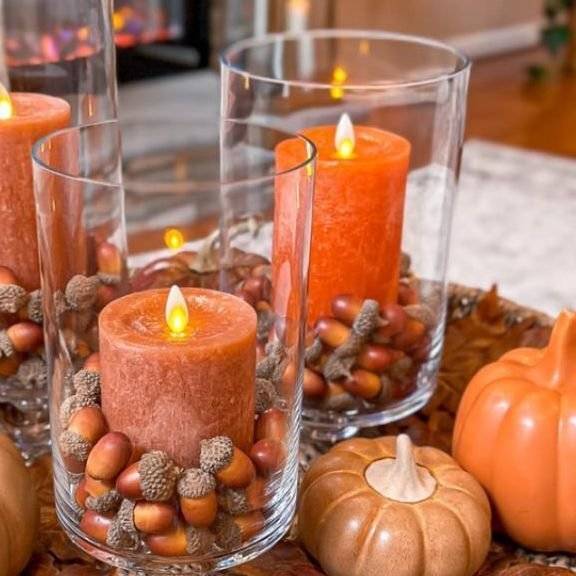 A fall vase with acorns and orange candles.