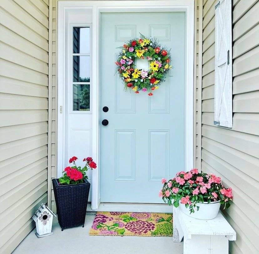 A blue door with a floral wreath and flowers.