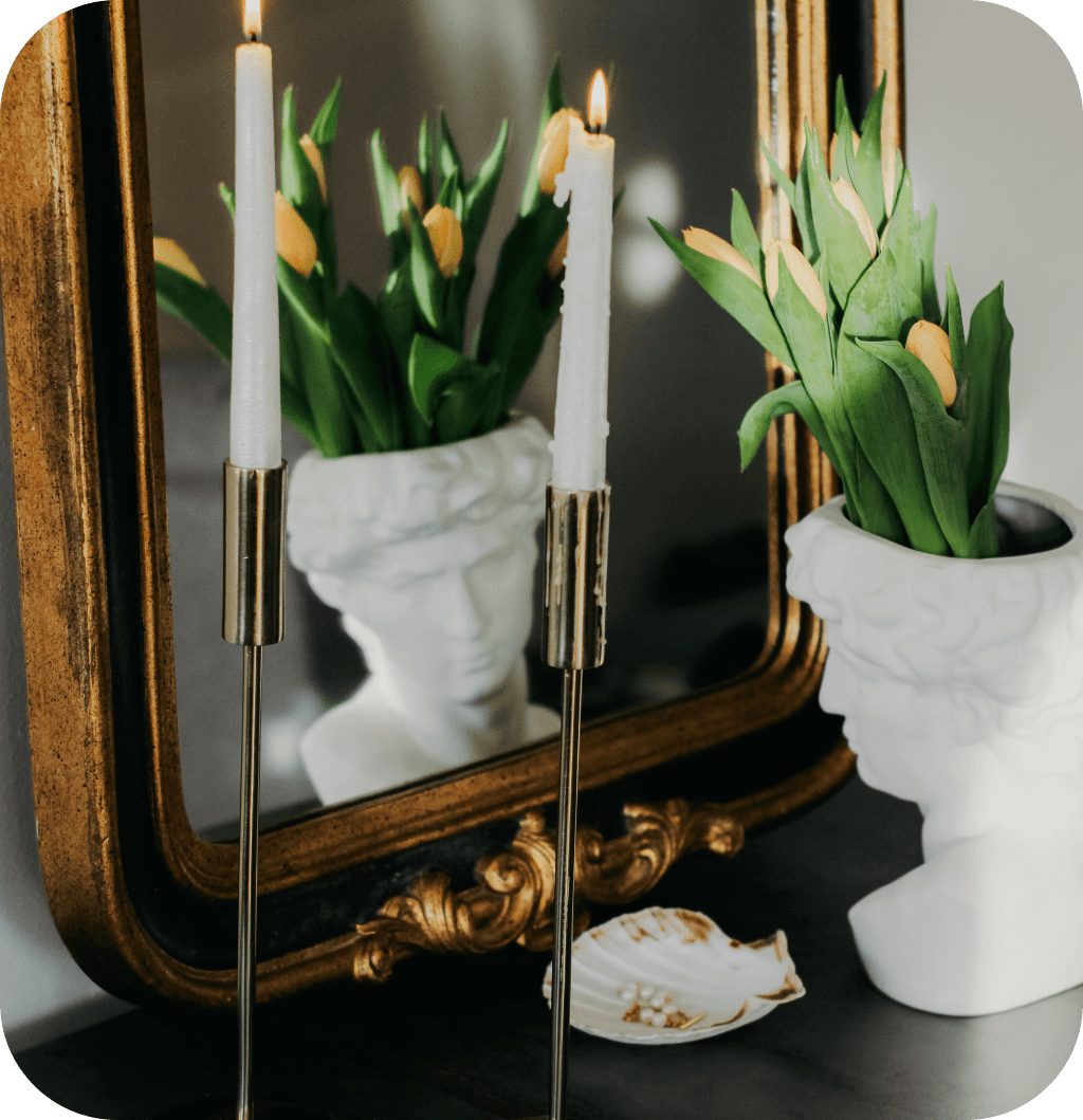 A gold mirror on top of a black console table with a vase and candles.