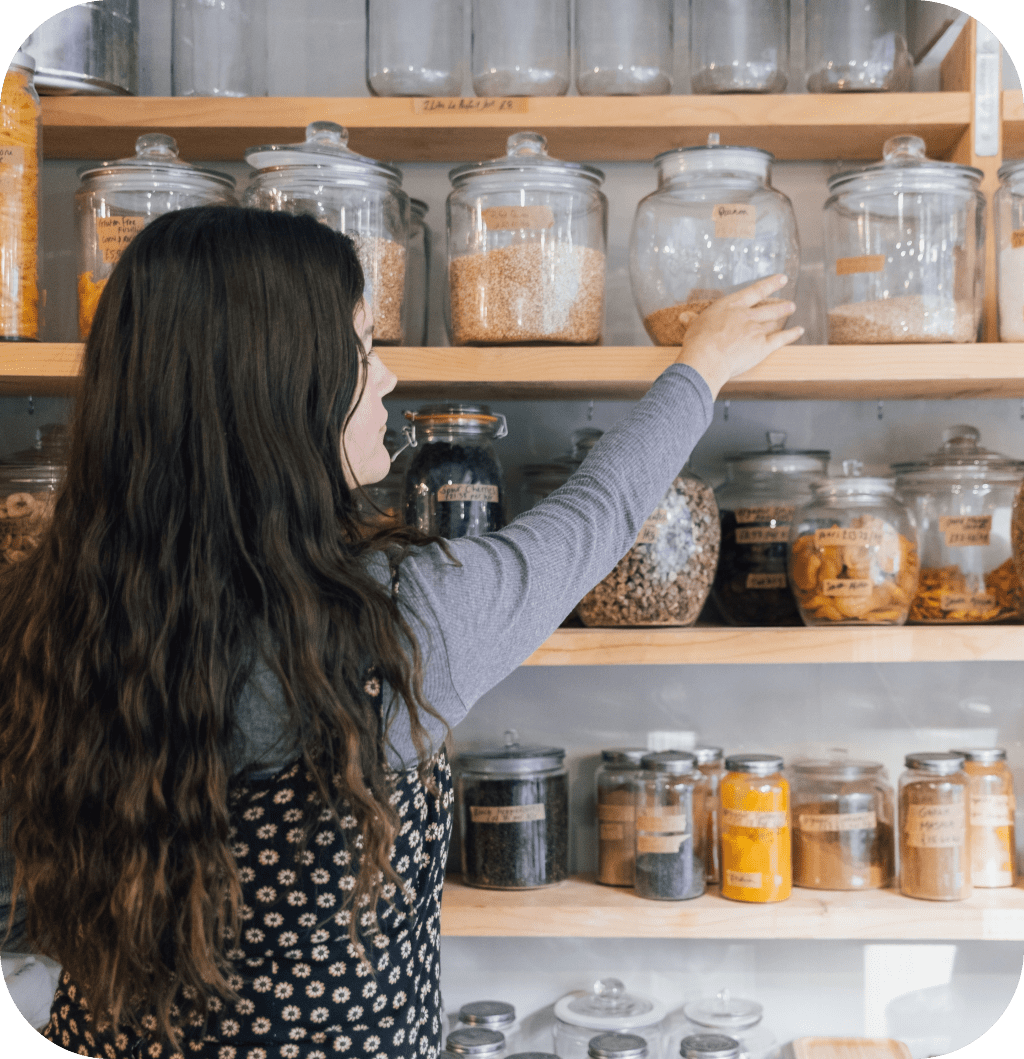 A woman taking a glass jar on a wooden shelf.