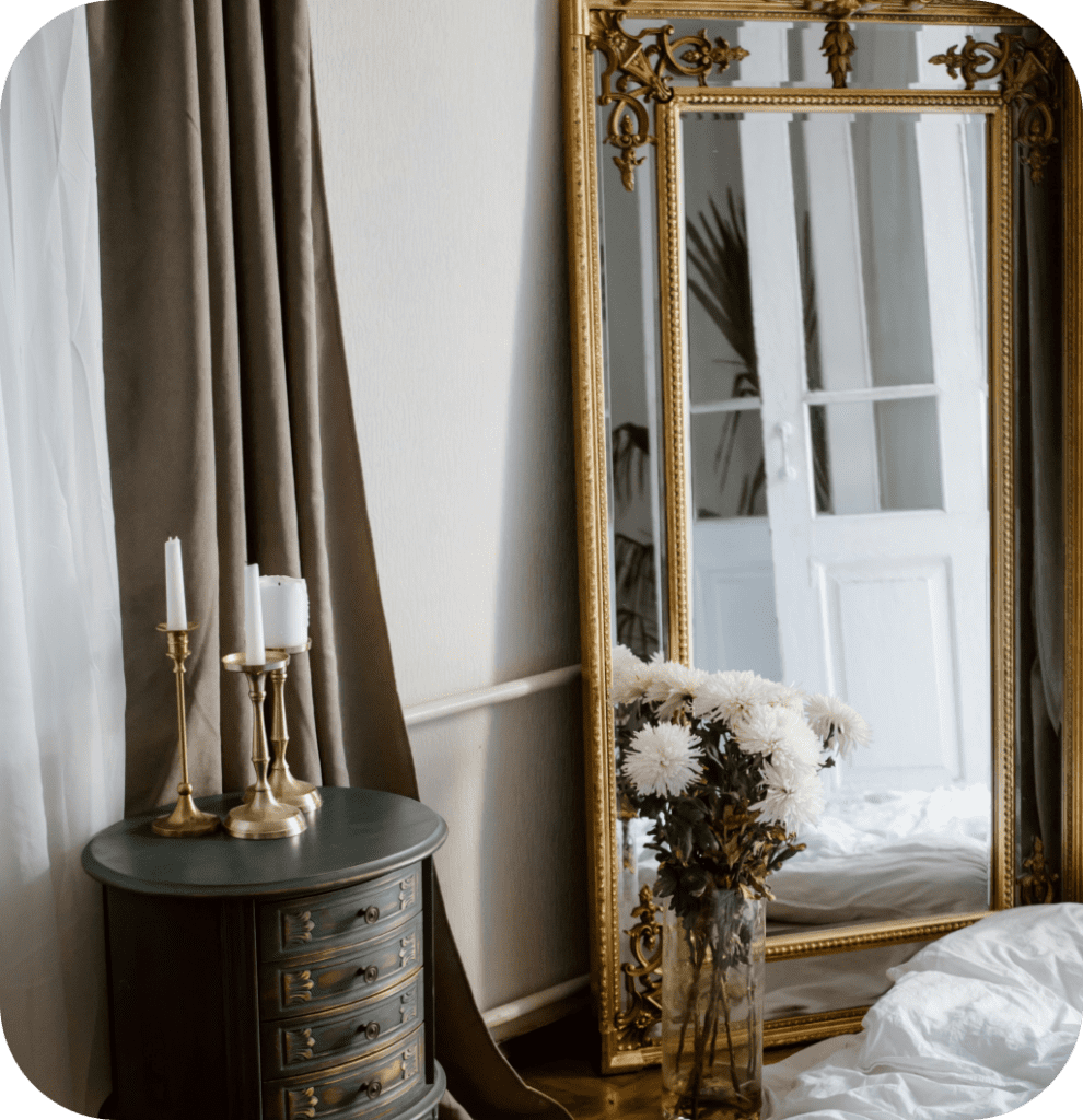An intricate golden mirror with flowers and a white bed.