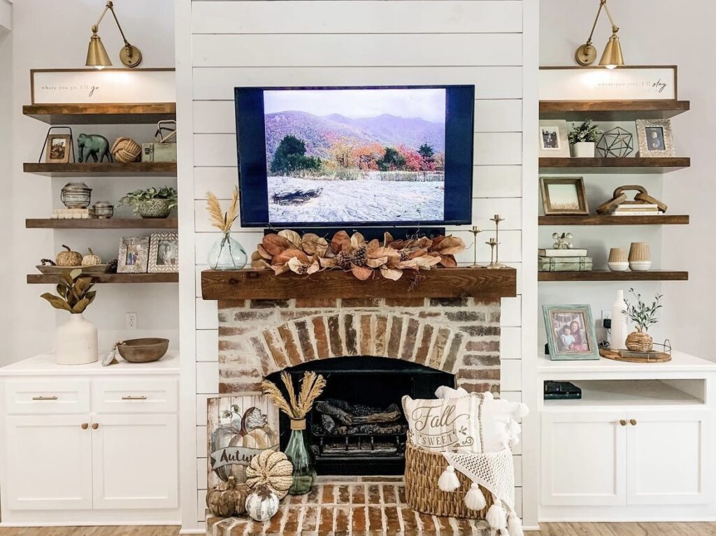 A mantel with fall leaves, pine cones, pumpkins and pillows.