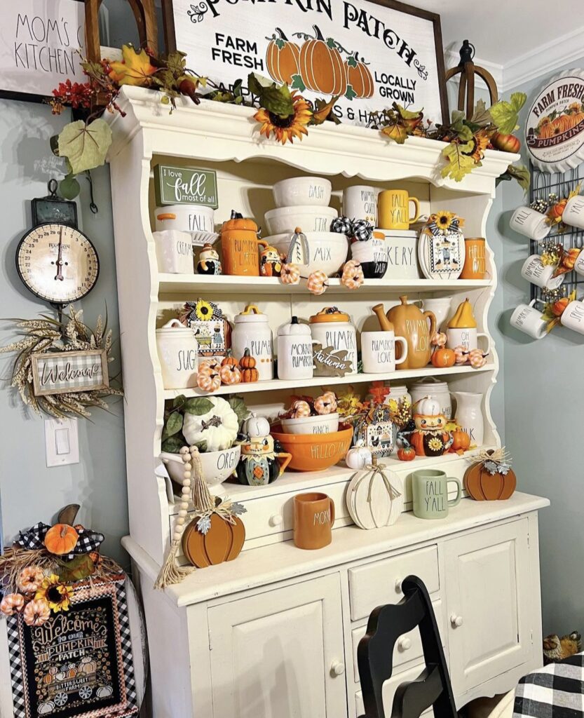 A white shelf filled with fall mugs and a maple leaf garland.