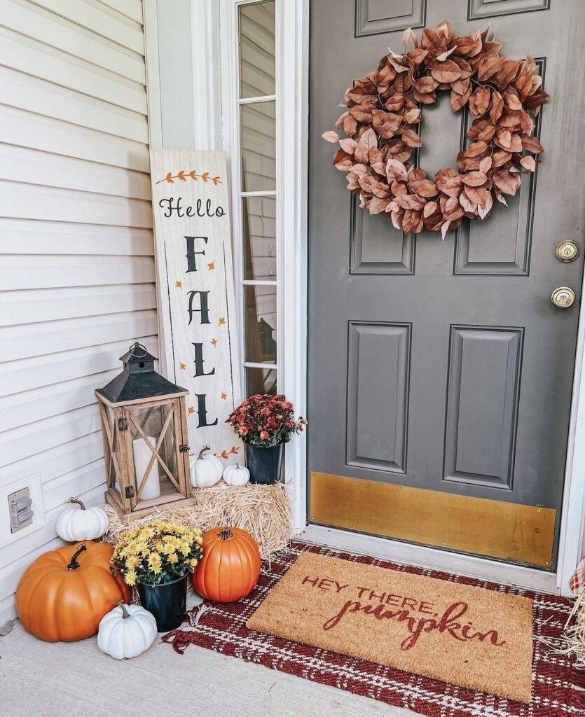 A fall sign with pumpkins and a haystack on a fall porch.