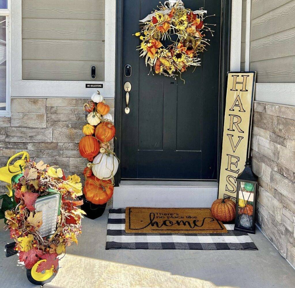 A fall porch with a harvest sign, pumpkins and a lantern.