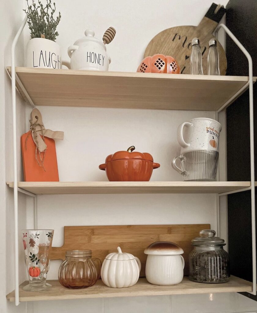 A kitchen shelf filled with fall mugs and pumpkin bowls.